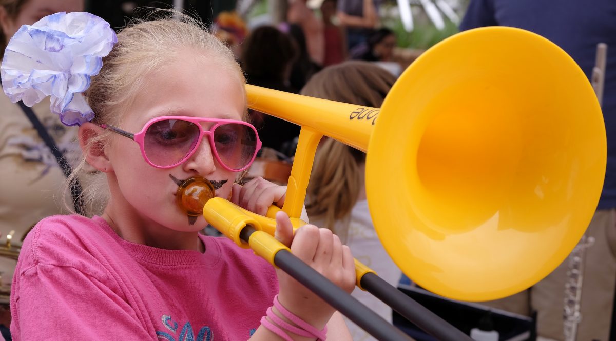 A girl wearing pink glasses playing a plastic, yellow trombone.