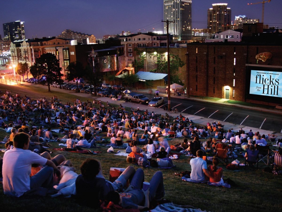 People in a city sit on blankets in a park and watch an outdoor film.