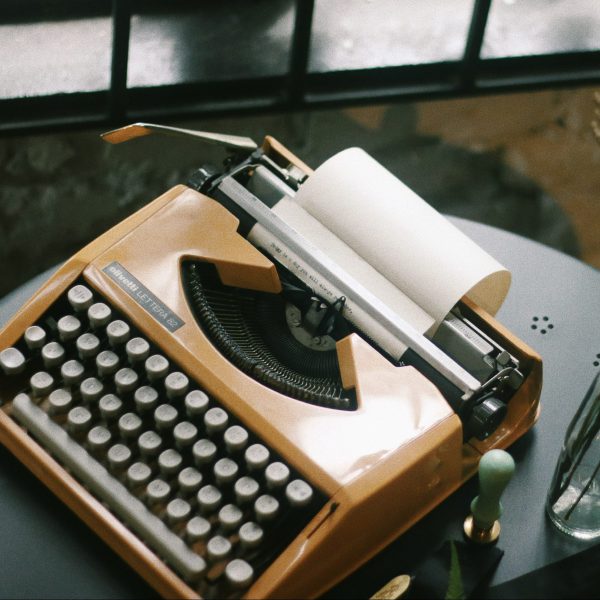 An orange typewriter sits on a dark table.