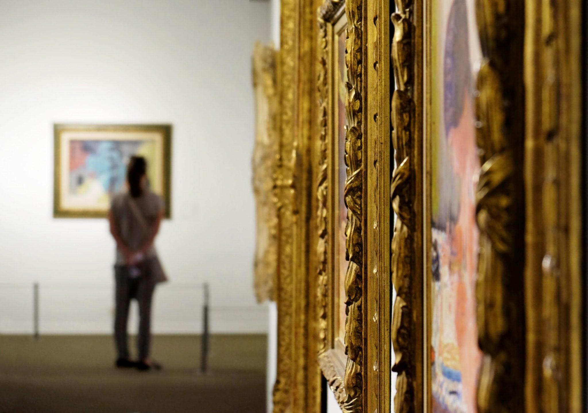 Golden, ornate frames in an art gallery with a person standing in the distance.