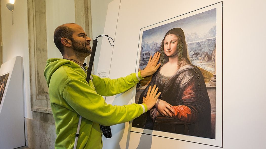 A blind man interacts with a print of the Mona Lisa using his hands.
