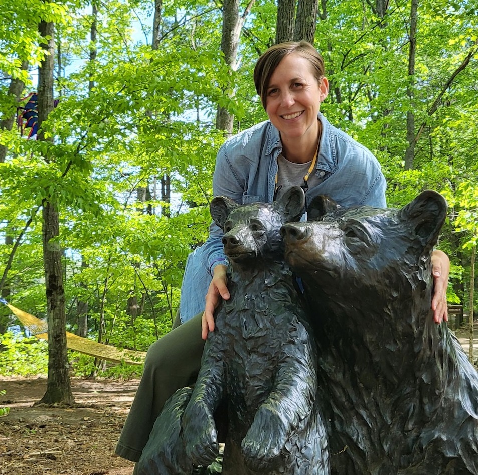 A woman poses with an outdoor sculpture of a mama bear and her cub.