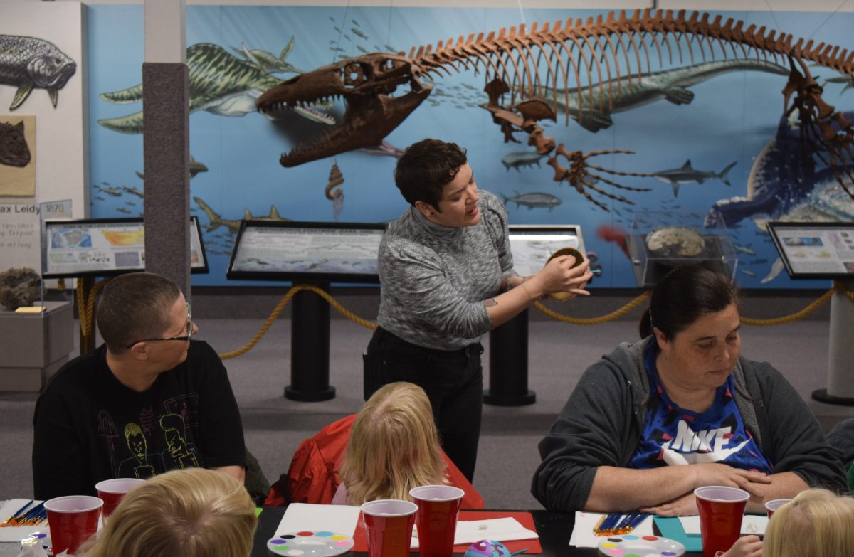 An instructor stands in a room with a science display of animal skeletons behind her, students in front of her
