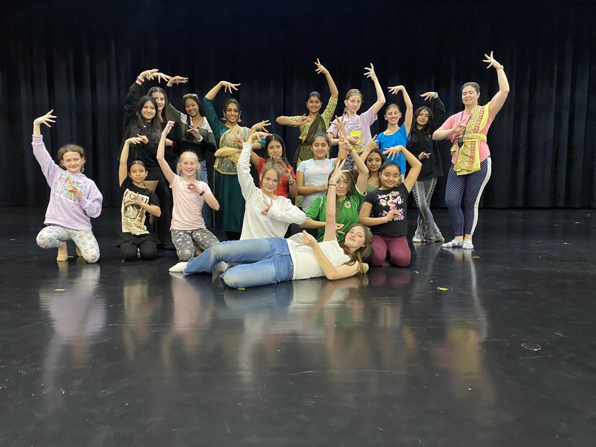Group of students pose with dance teacher, arms upraised in dance positions