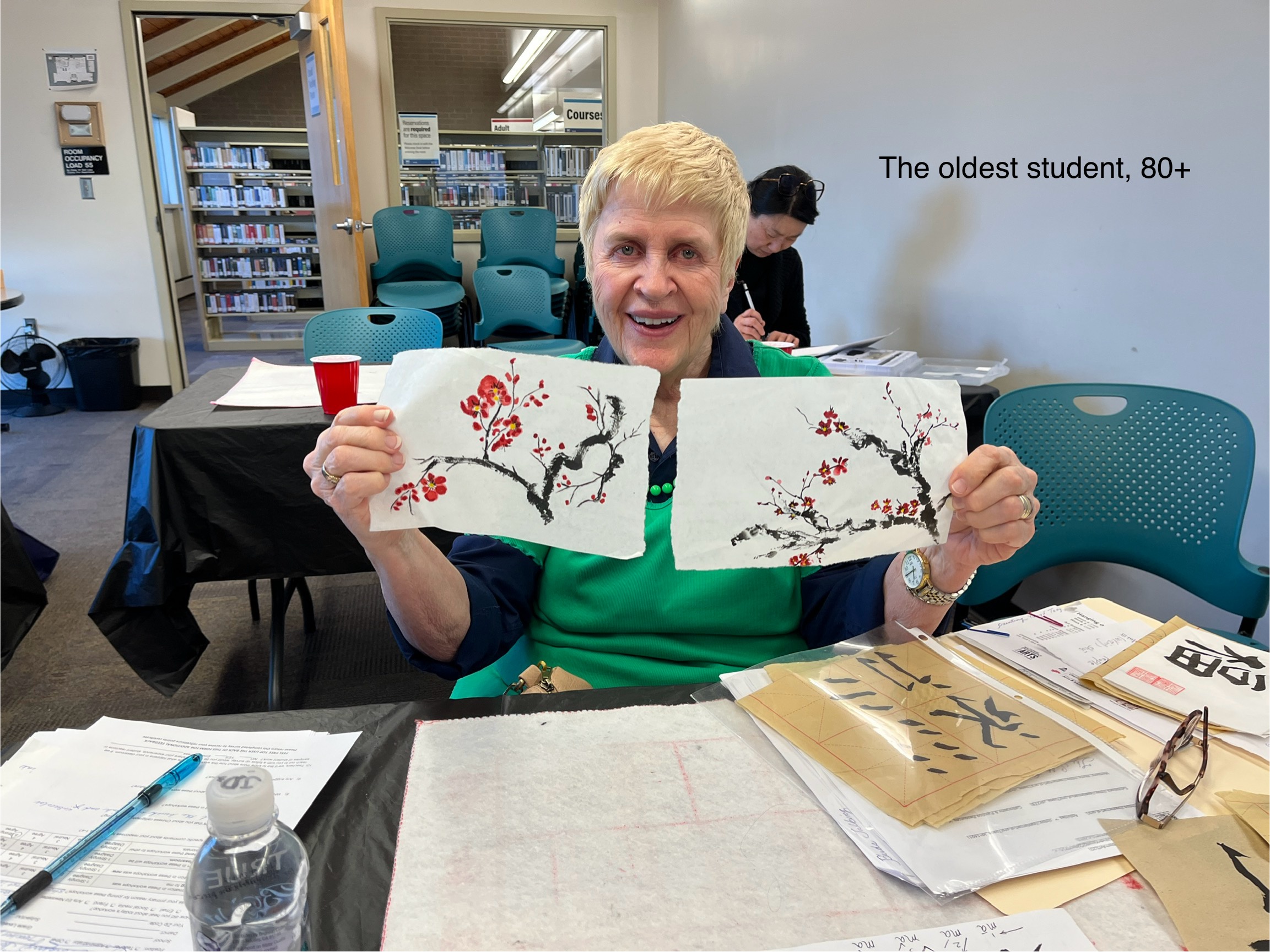 Senior woman smiles and holds up two examples of her paintings