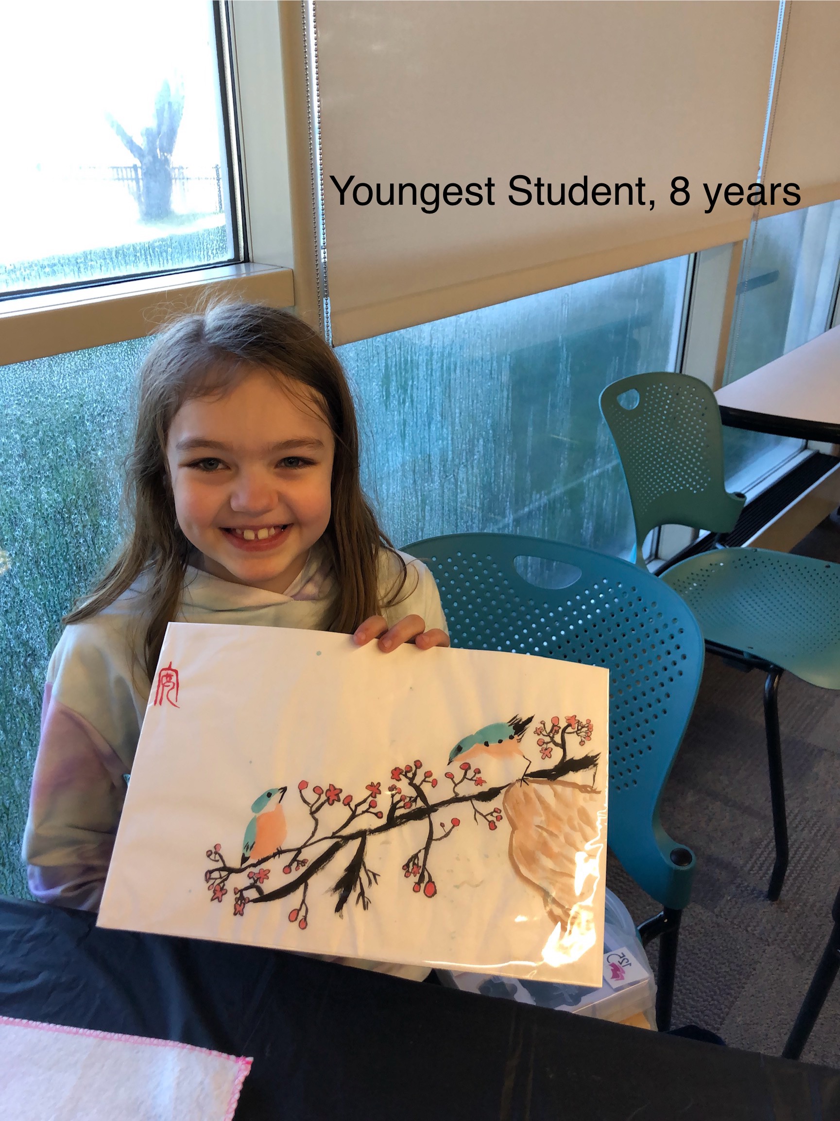 A young smiling girl holds her painting of a blossom branch up